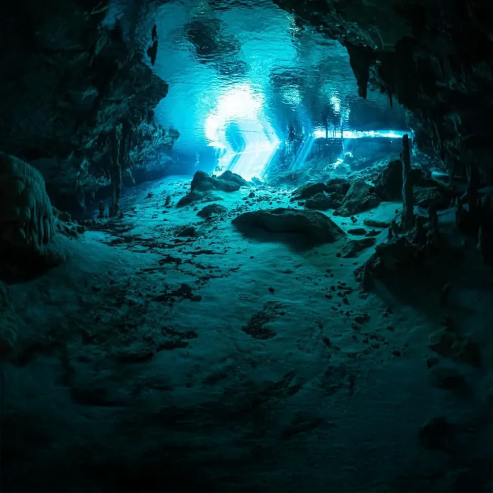 Divers by the lit entrance of the Cenote Angelita cavern
