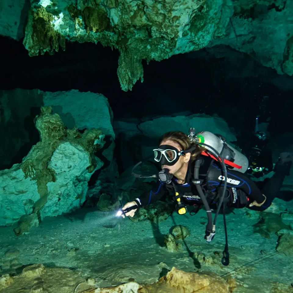 Diver lighting the rock formations under the cavern ceiling at Cenote Dos Ojos