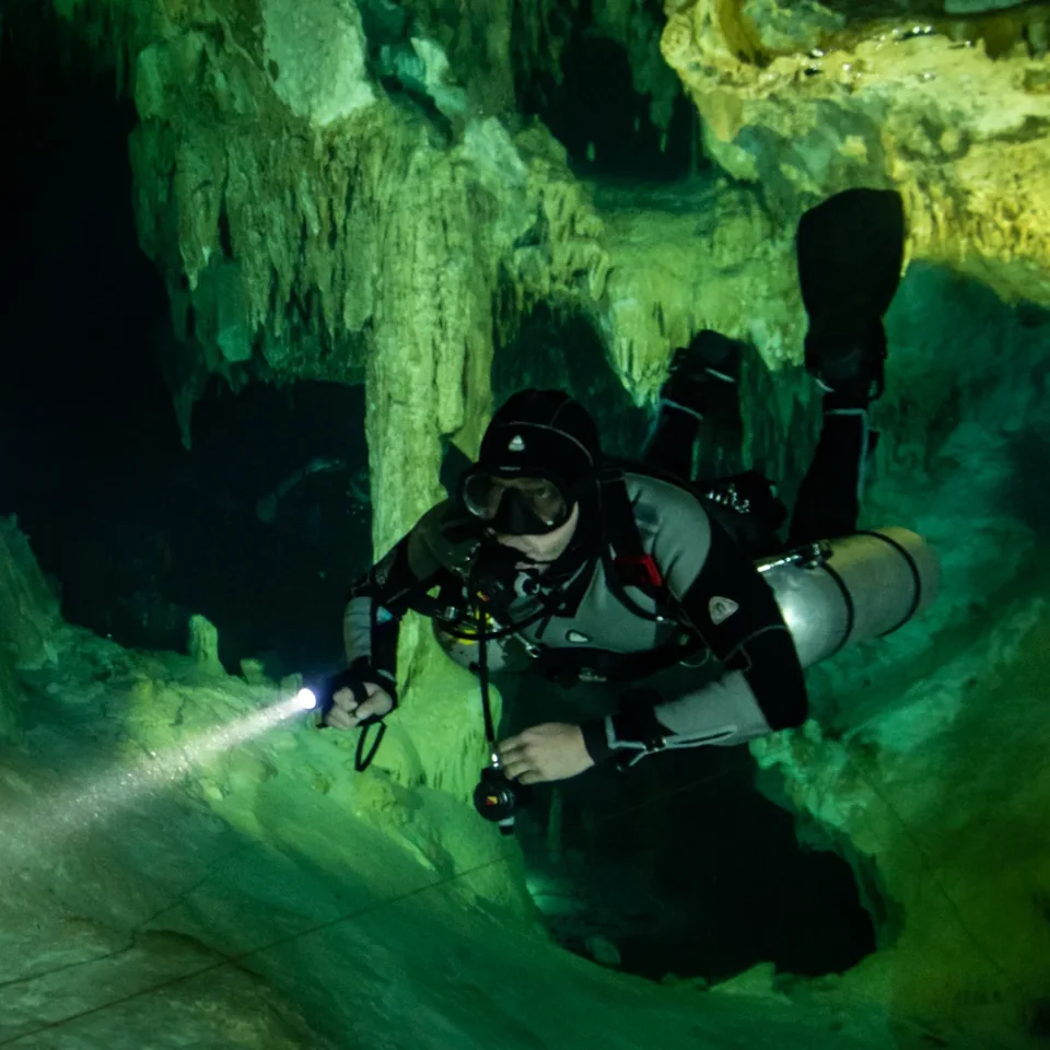 Diver with a torch gliding past the formations of Cenote Dream Gate