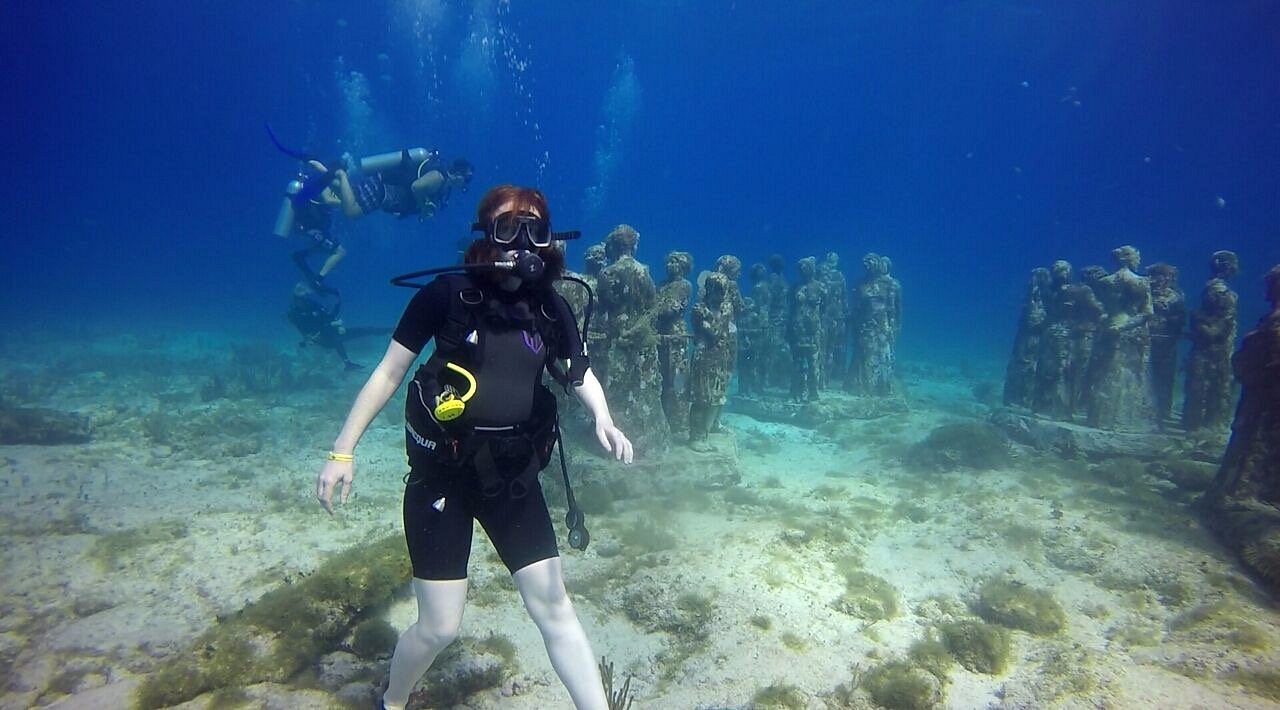 Diver hovering over the sand beside rows of submerged statues at the MUSA Cancun underwater museum