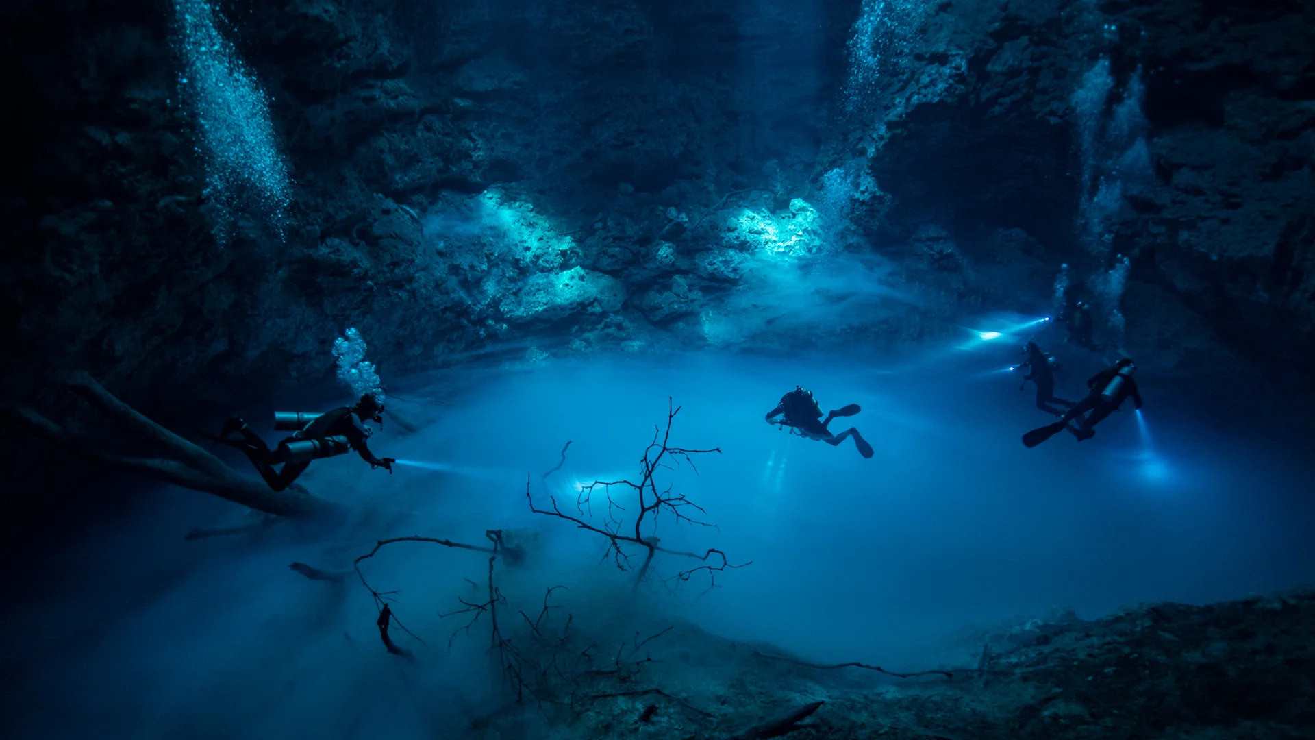 Sunlight beams illuminating the inside of a coral reef cavern filled with fish, a stunning view to experience while scuba diving in Cancun.